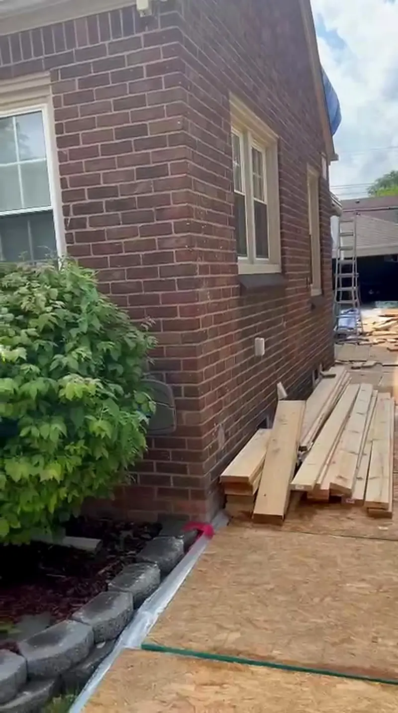 Lumber staged beside the brick home ahead of framing, Dearborn MI
