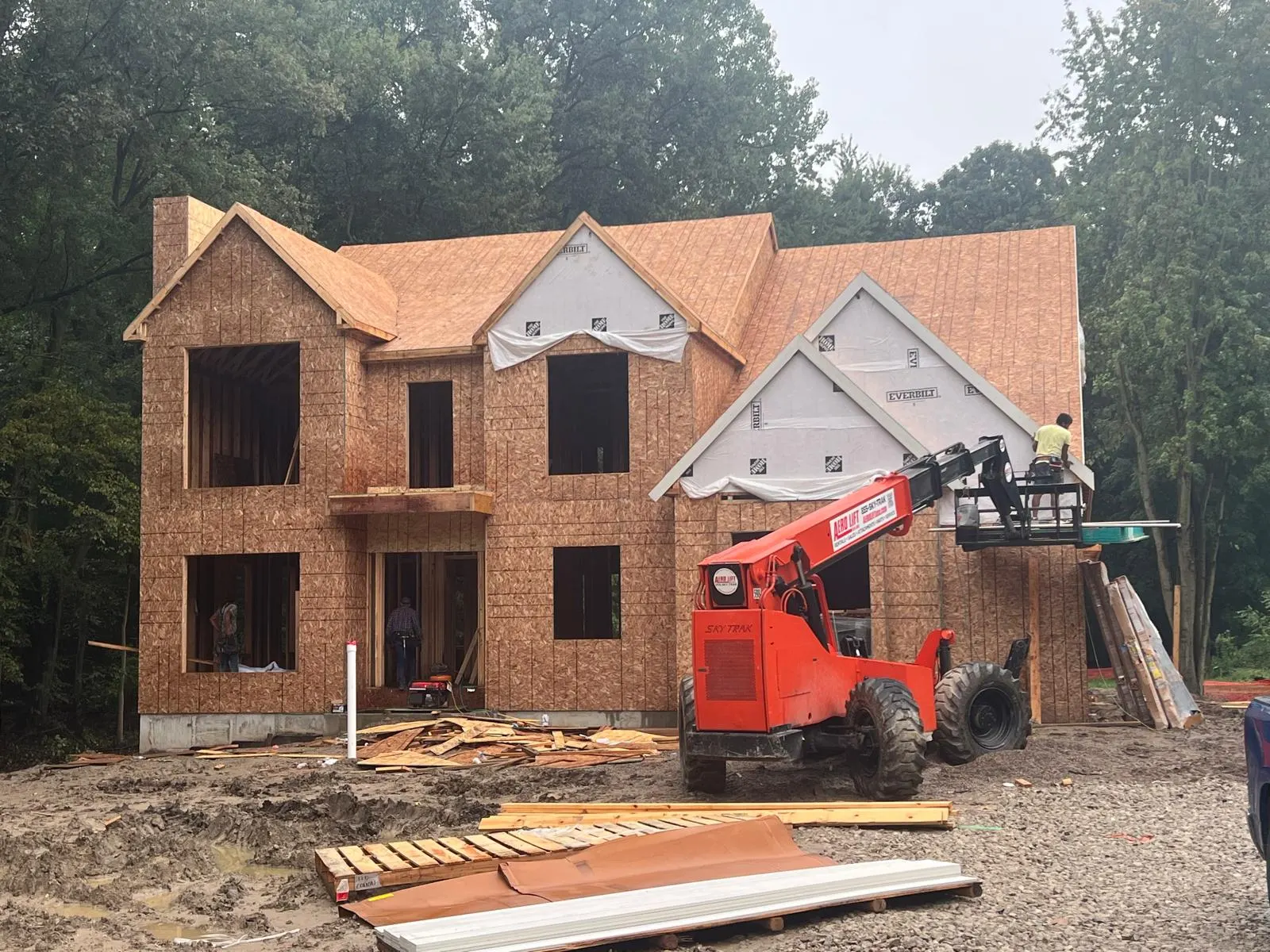 New custom home sheathed with the roof decked, telehandler working the front gable, under construction
